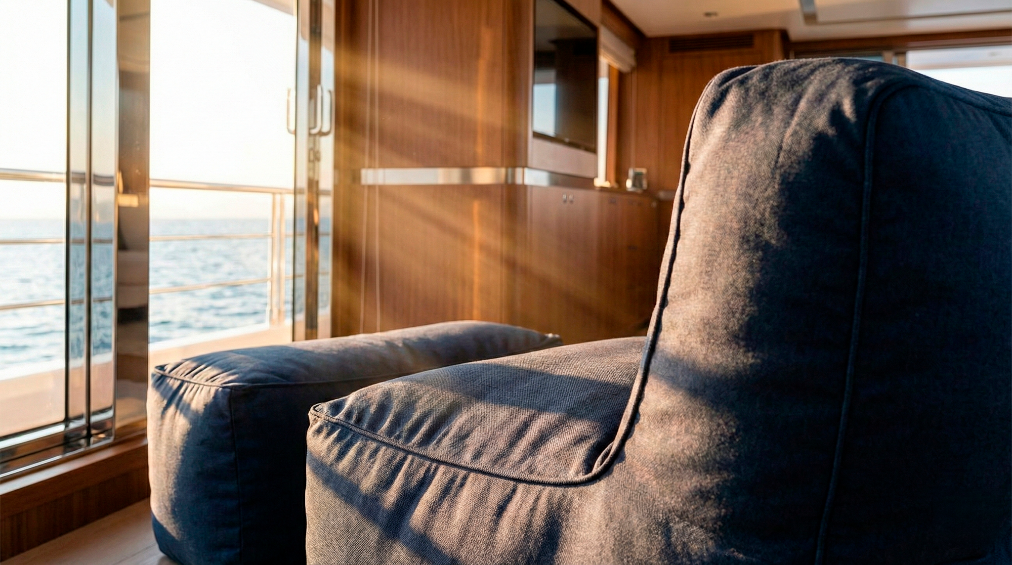 Dark gray armchair on a boat with wooden paneling and glass windows showing water.