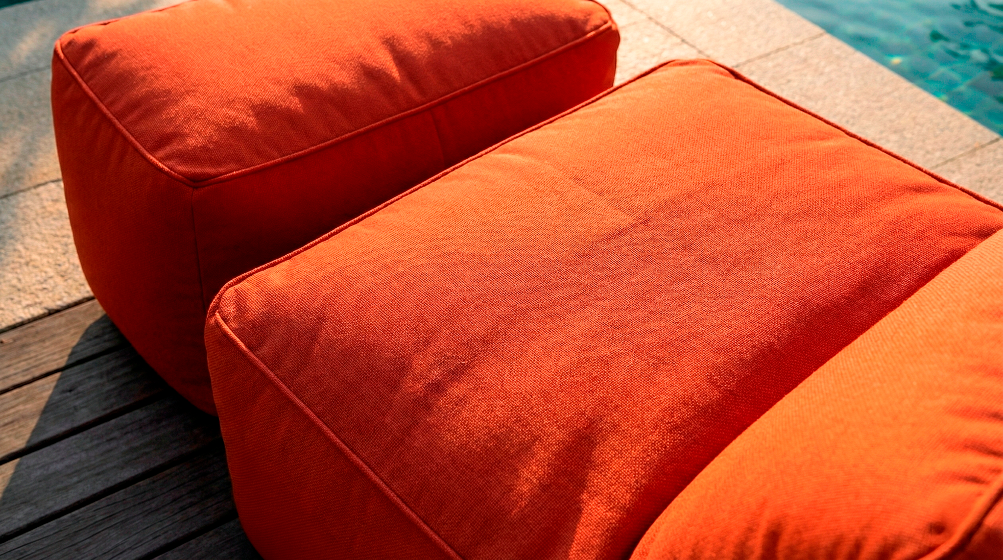 Two orange cushions on a wooden deck near a pool.