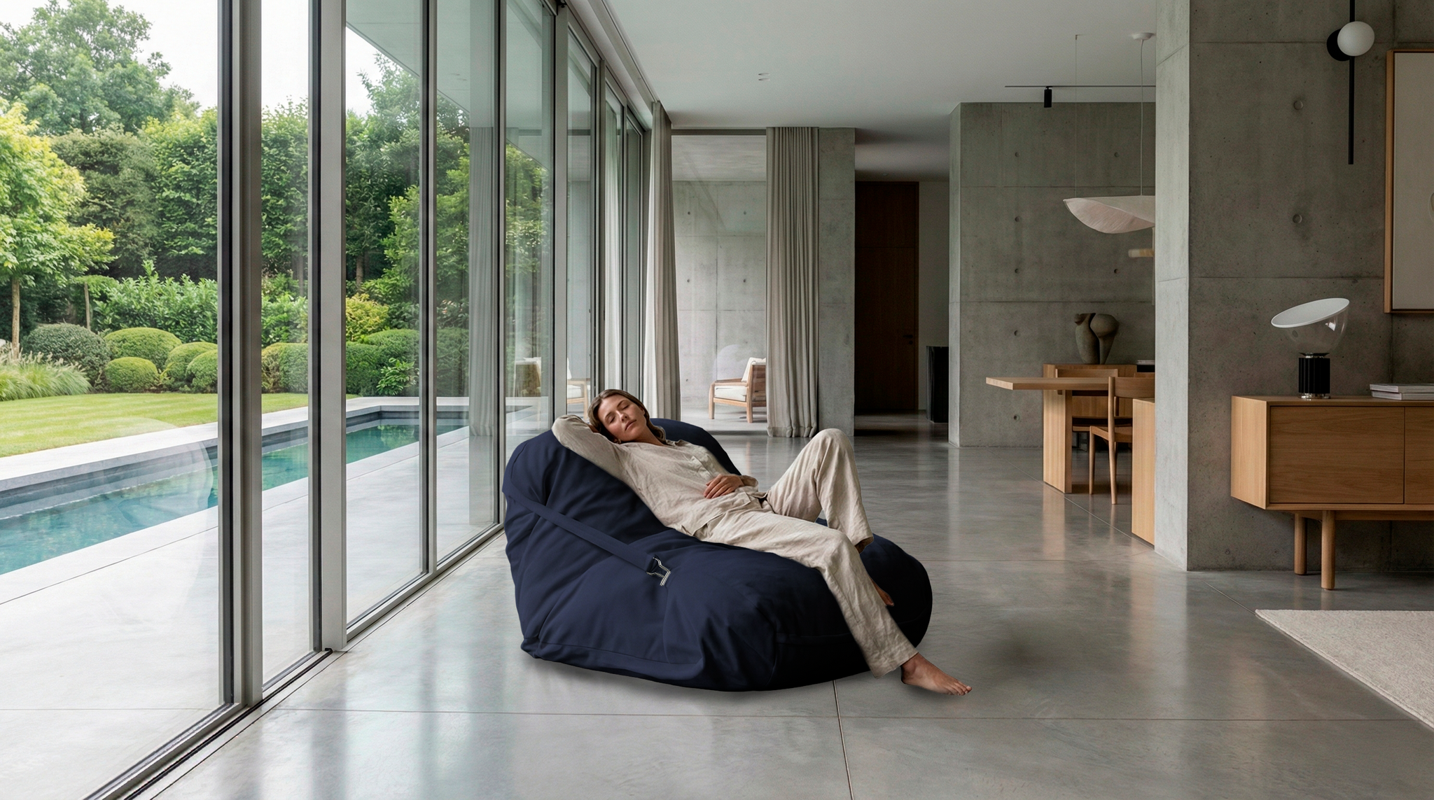 Person relaxing in a bean bag chair by a poolside in a modern home.