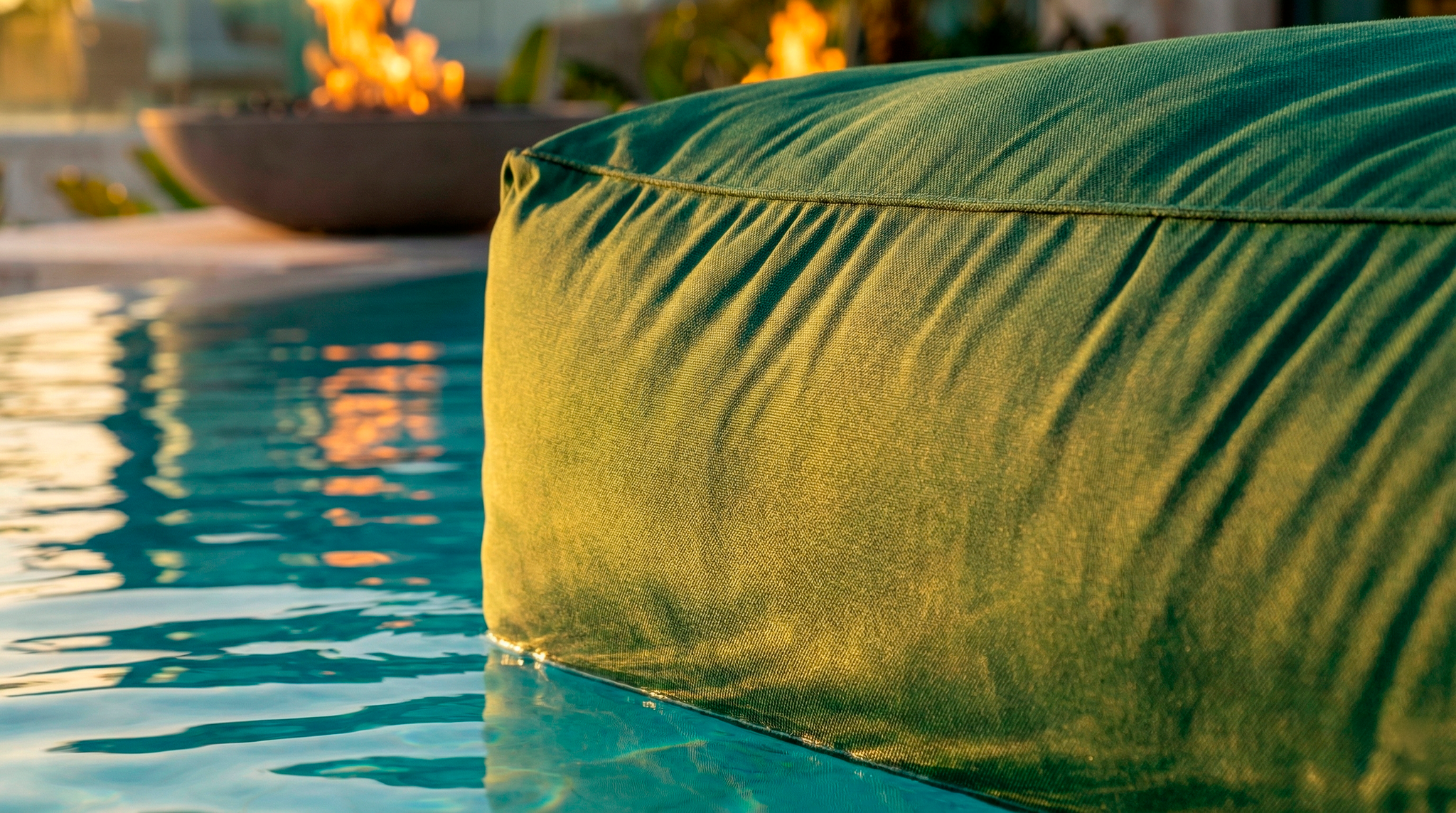Green cushioned chair by a pool with flames in the background